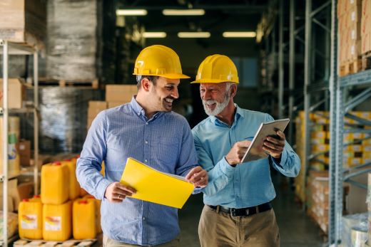 Two men with hard hats looking at a tablet walking through a warehouse.