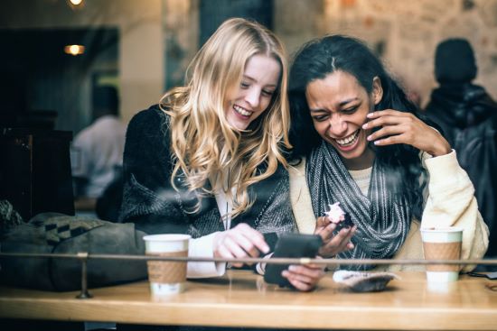 Two girls laughing while looking down at a smartphone.